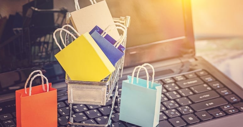 Bolsas y carrito de compras sobre laptop simbolizando las ventas de tercerizar un ecommerce